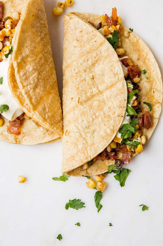 Three vibrant vegan tacos on a rustic ceramic plate, filled with roasted sweet potatoes, black beans, avocado, red cabbage, and pickled onions, styled naturally.