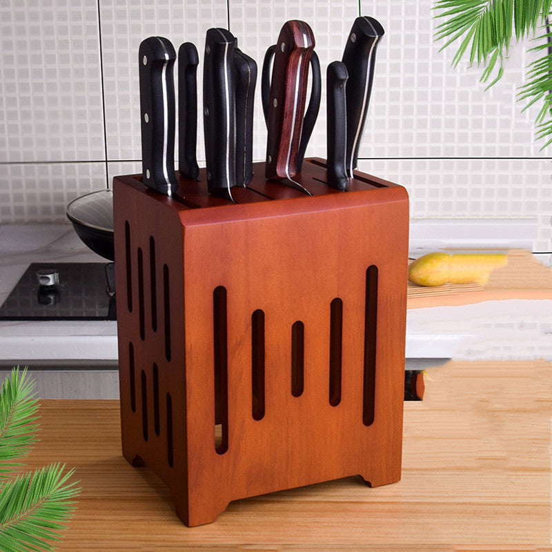 A wooden knife holder with multiple slots, containing various kitchen knives, displayed on a table with a partial view of a banana and some kitchen appliances in the background.