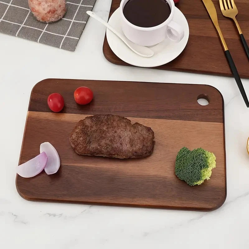Wooden cutting board with a steak, tomatoes, broccoli, and onion on a marble surface.