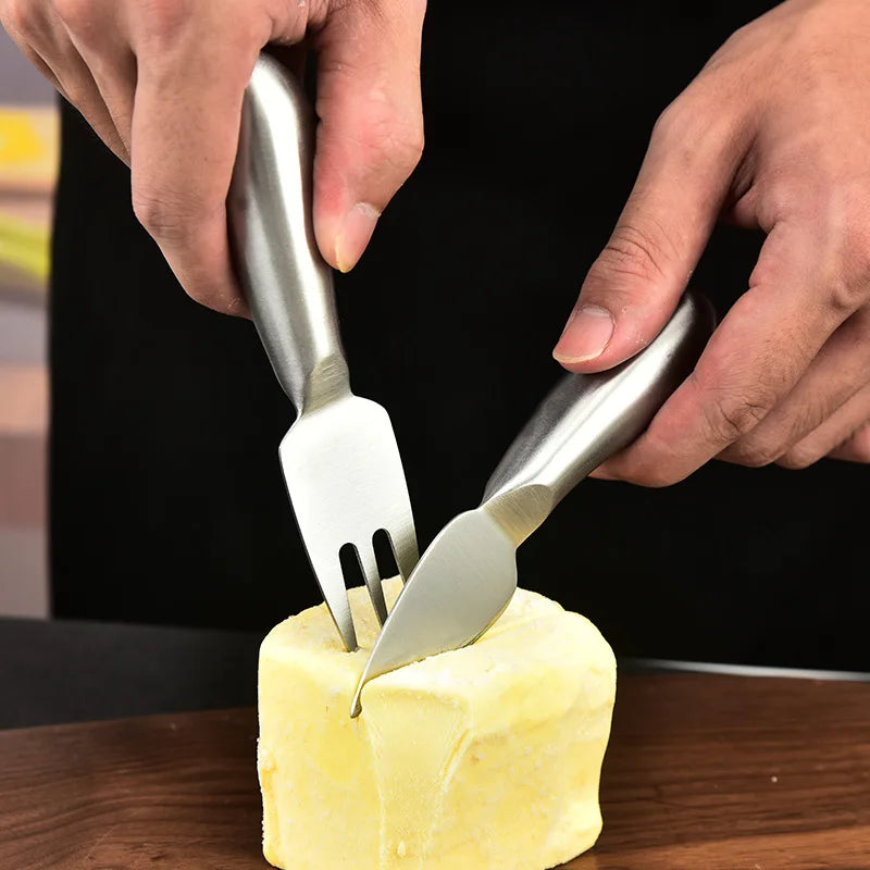 Two metal utensils cutting into a block of butter on a wooden surface.