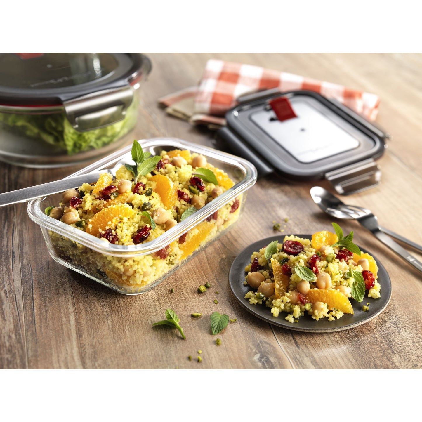 Salad in a clear container on a wooden table with a checkered cloth in the background