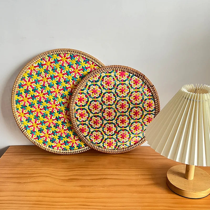 Two colorful woven trays with a geometric pattern on a wooden surface next to a lamp.