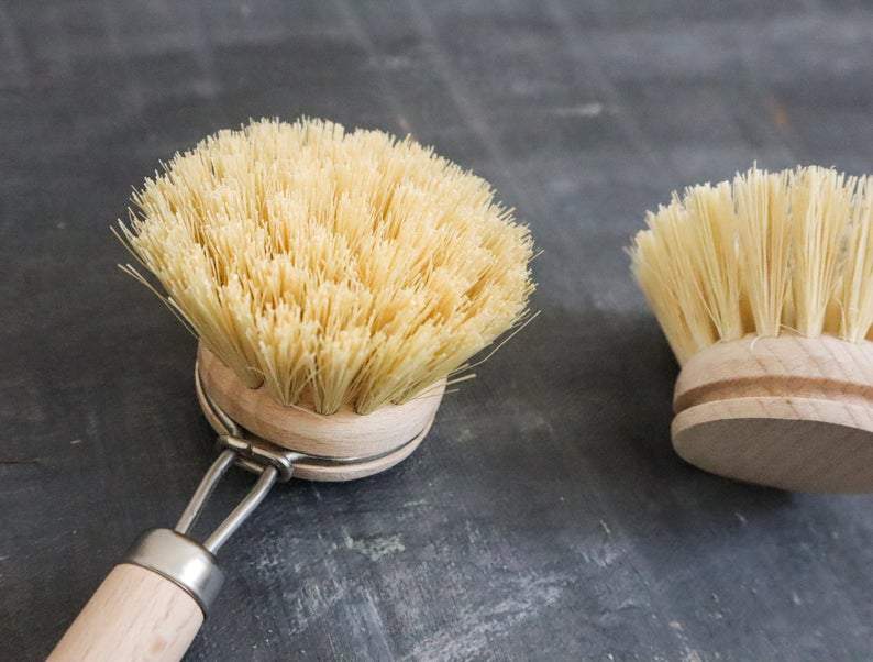 Two dish brushes with natural bristles on a dark surface