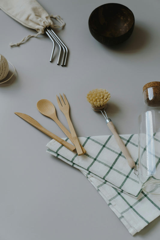 A stylish eco-friendly dining setup featuring bamboo plates, stainless steel utensils, and glass cups, promoting a sustainable and waste-free lifestyle.