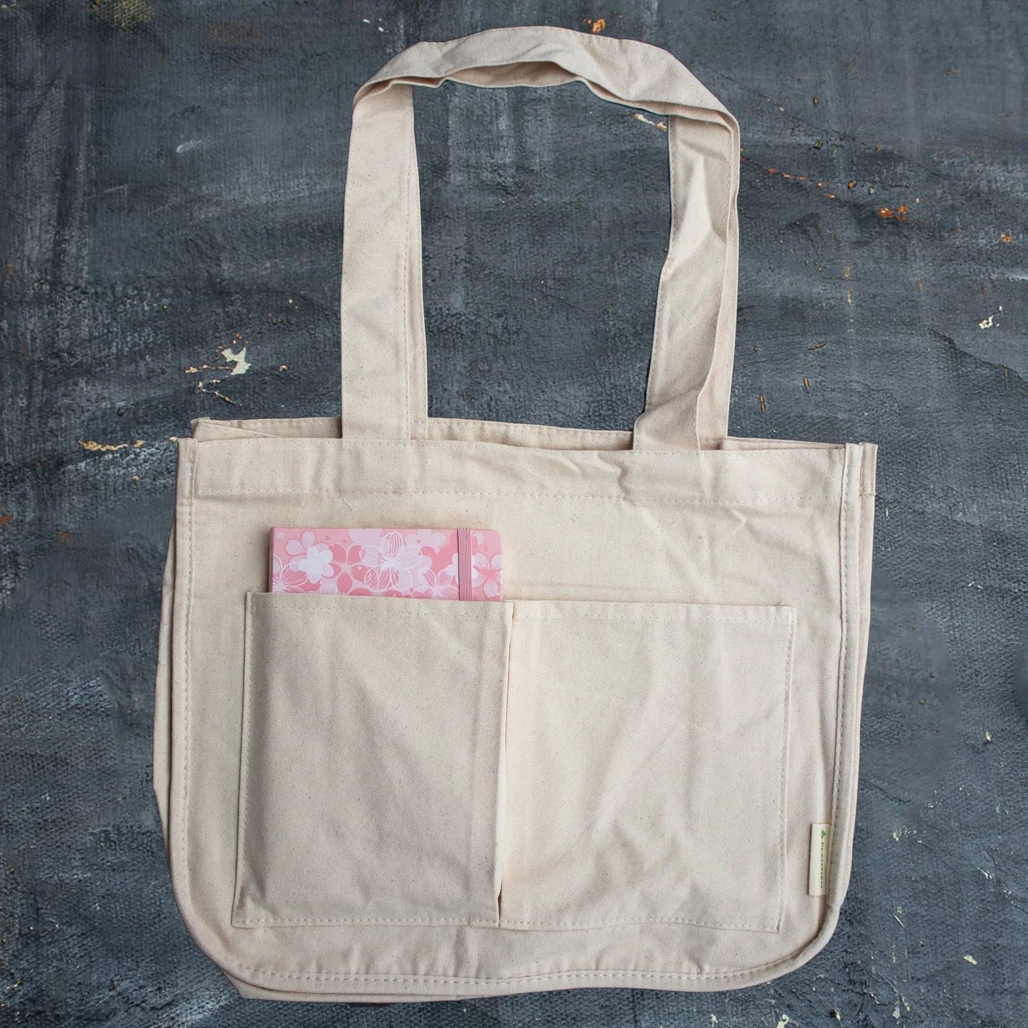 Beige tote bag with a pink floral pocket on a dark textured surface