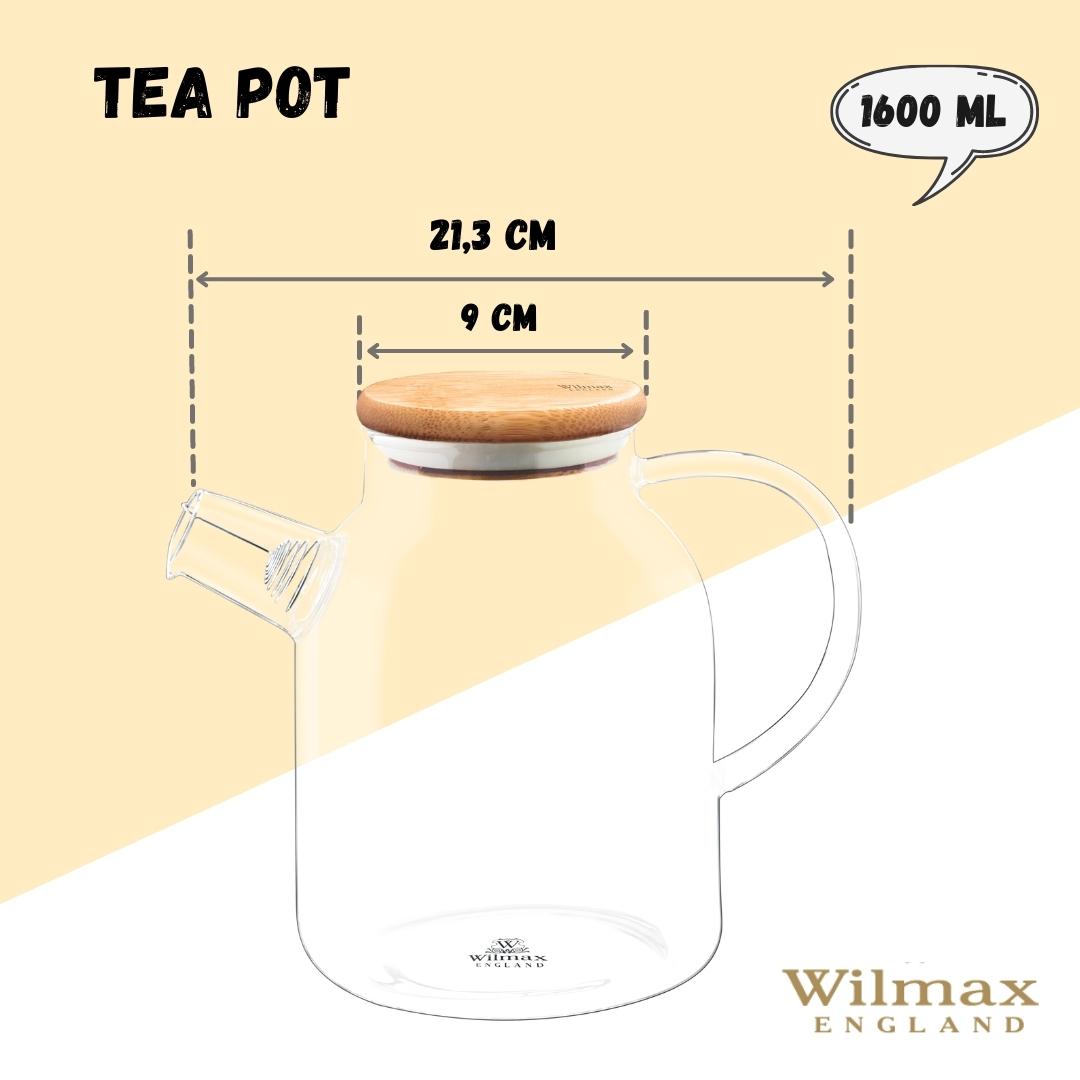 A clear glass teapot with a bamboo lid and stainless steel infuser, filled with golden-colored tea. The teapot has an ergonomic handle and is sitting on a wooden surface next to fresh tea leaves and a cup of tea.