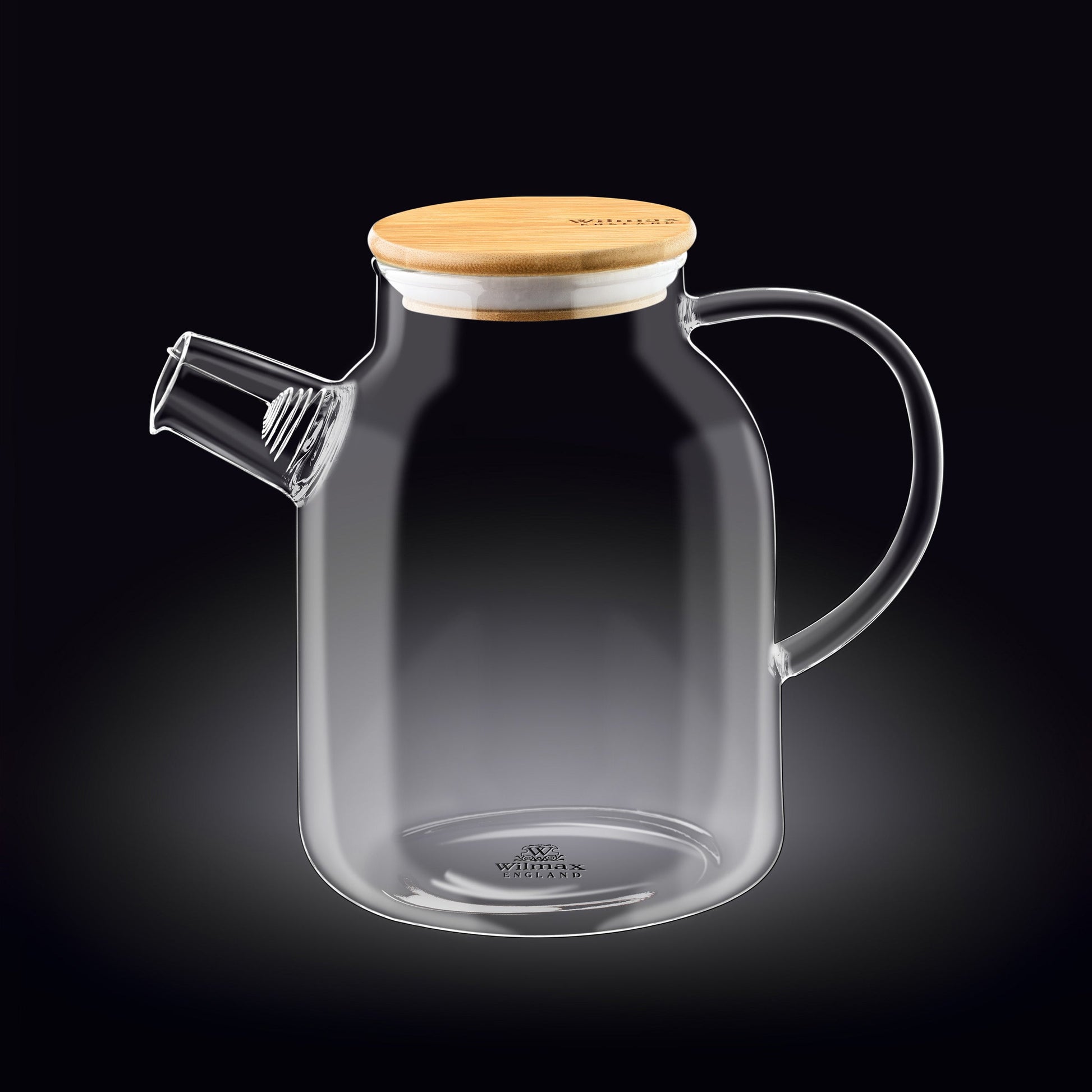 A clear glass teapot with a bamboo lid and stainless steel infuser, filled with golden-colored tea. The teapot has an ergonomic handle and is sitting on a wooden surface next to fresh tea leaves and a cup of tea.