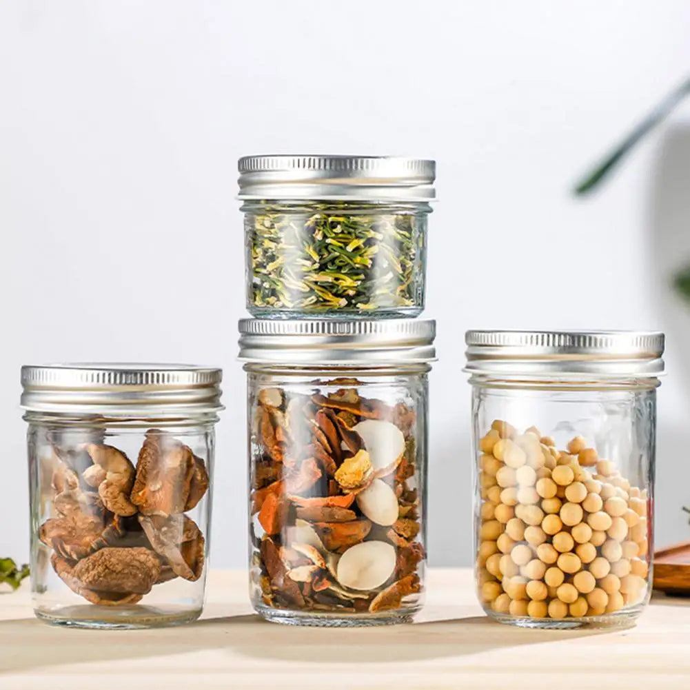 Set of glass jars with metal lids containing various items on a light surface.