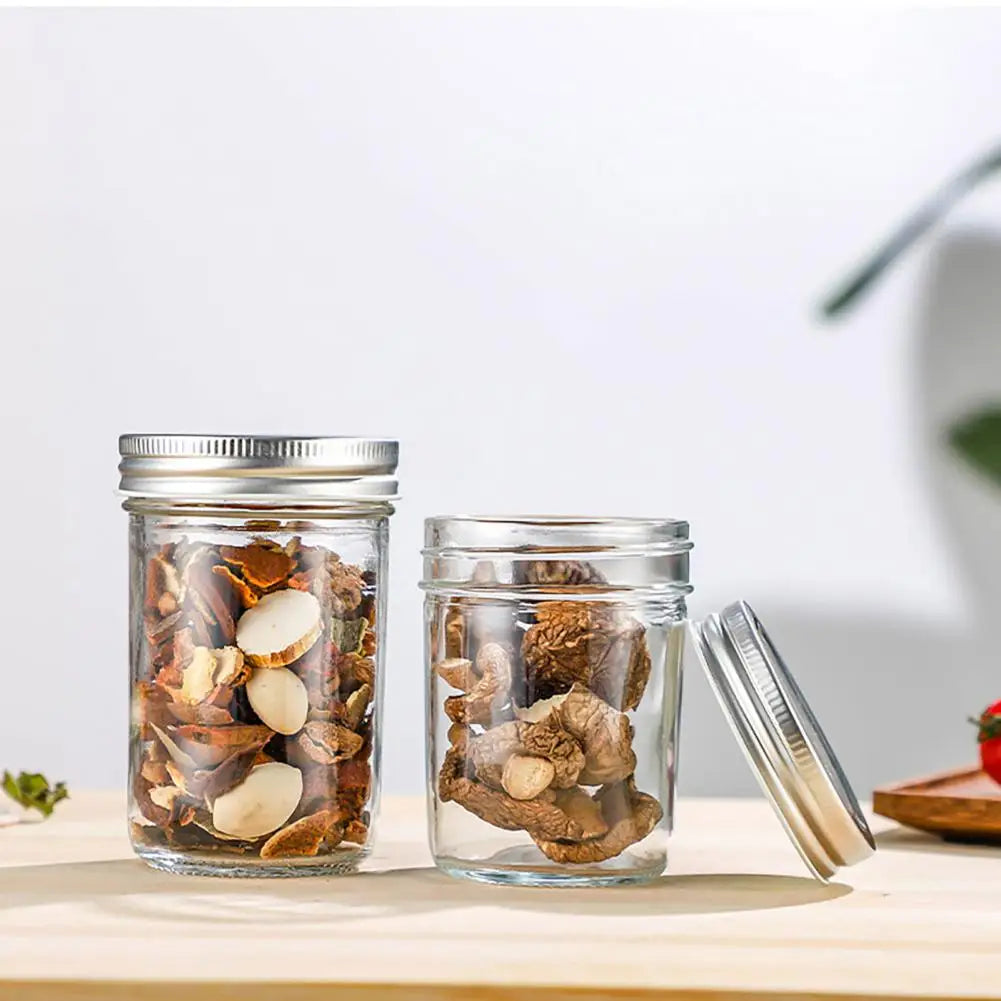 Two glass jars with metal lids on a wooden surface, containing various seeds and grains.