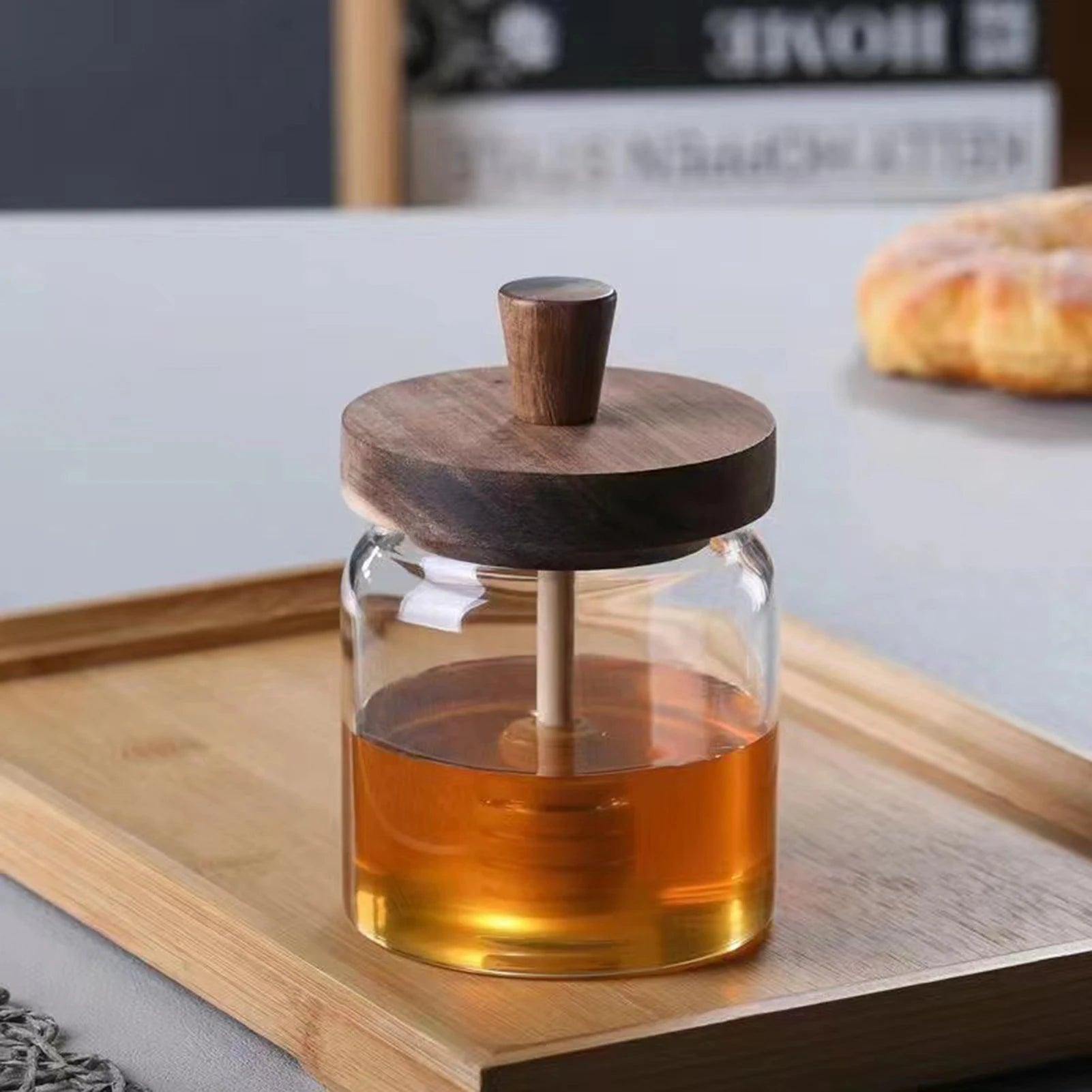 Glass jar with wooden lid containing a liquid on a wooden tray.