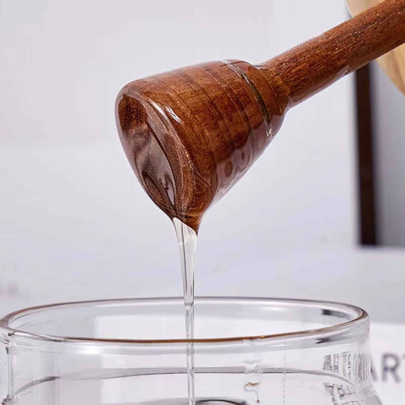 Wooden honey dipper pouring honey into a glass container with a blurred background