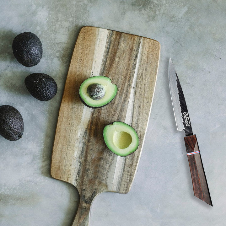 Avocados on a wooden cutting board with a knife on a concrete surface