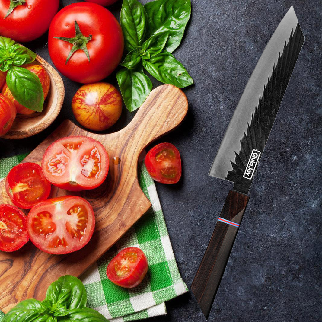 Wooden cutting board with sliced tomatoes, whole tomatoes, and basil leaves on a checkered cloth, with a knife on a dark surface.