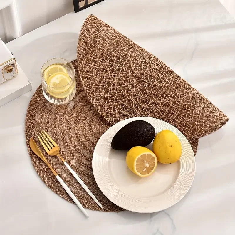 Table setting with a woven placemat, plate with avocado and lemons, and cutlery on a white surface.