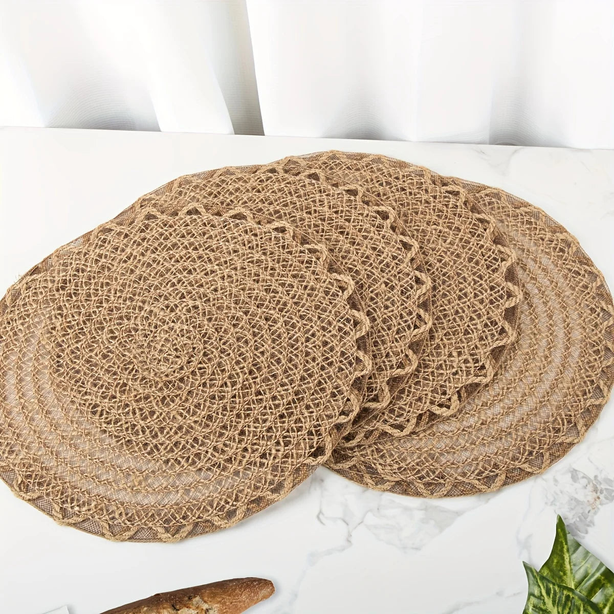 Set of burlap placemats on a white surface with a plant in the corner.