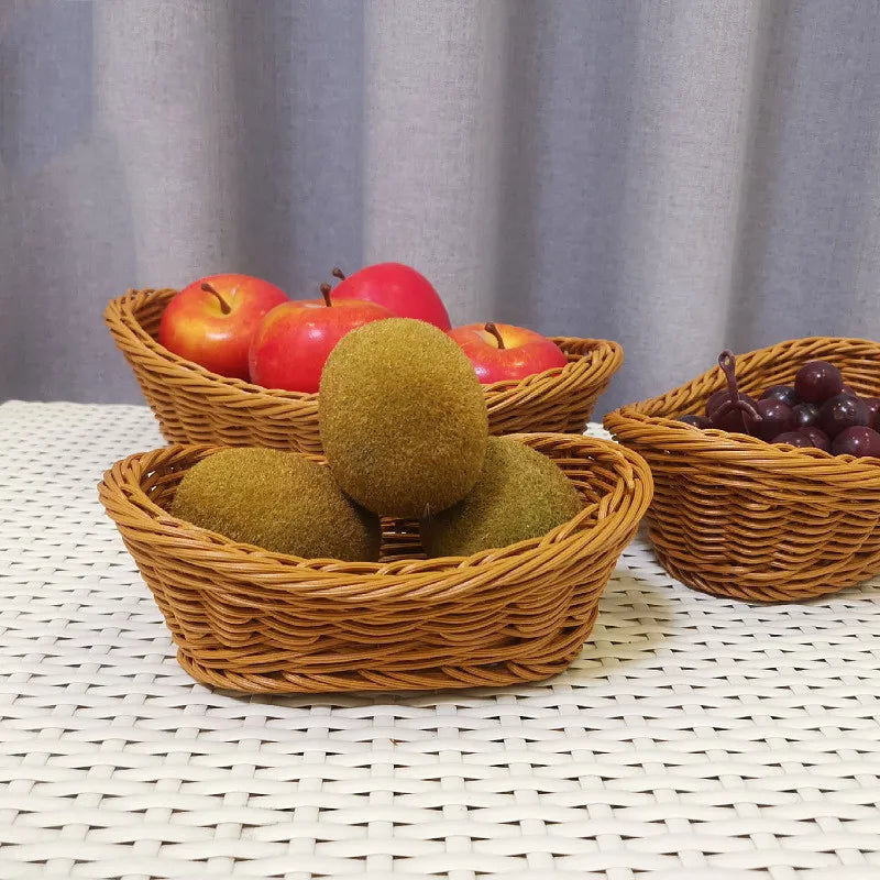 Three woven baskets containing apples, kiwis, and grapes on a white surface with a gray curtain background.