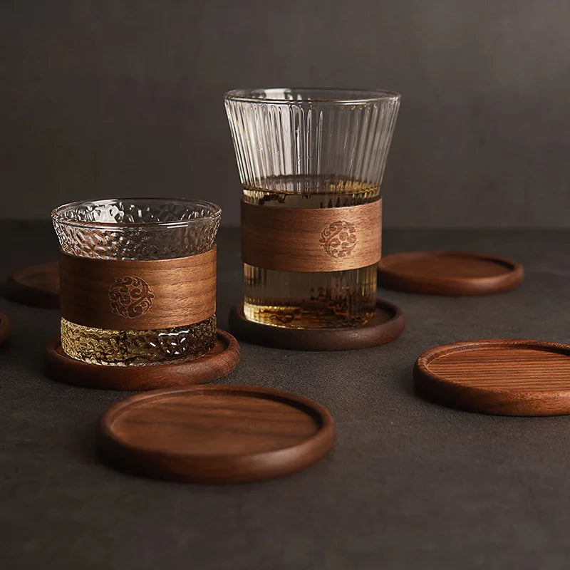 Two glass cups with wooden accents and coasters on a dark surface