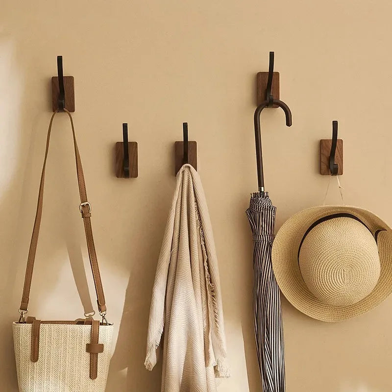 Set of wooden wall hooks with a bag, towel, umbrella, and hat on a beige wall.