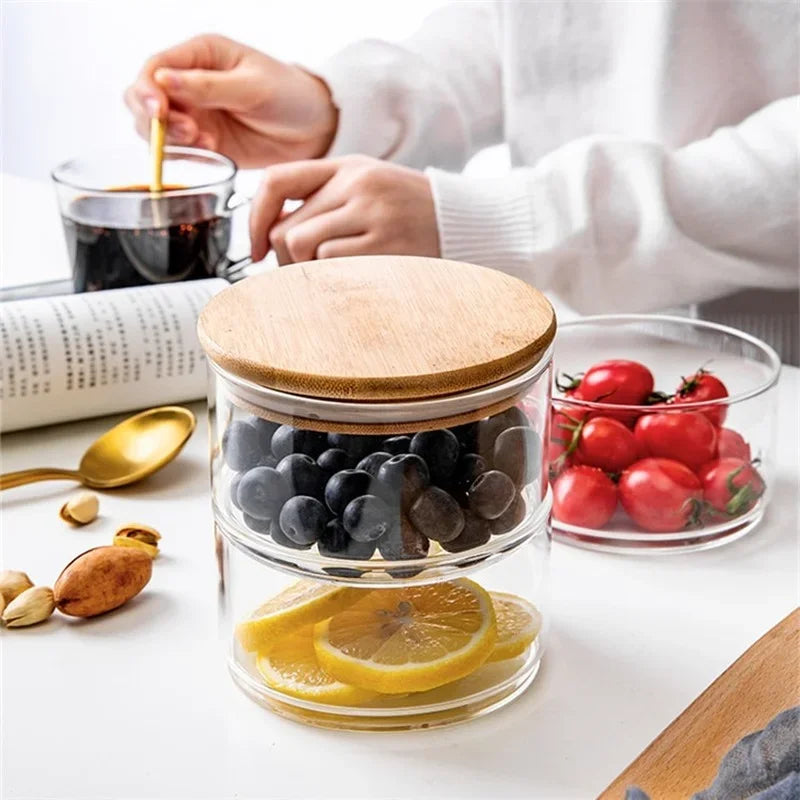 Glass jar with wooden lid on a table with fruits and a cup of coffee.