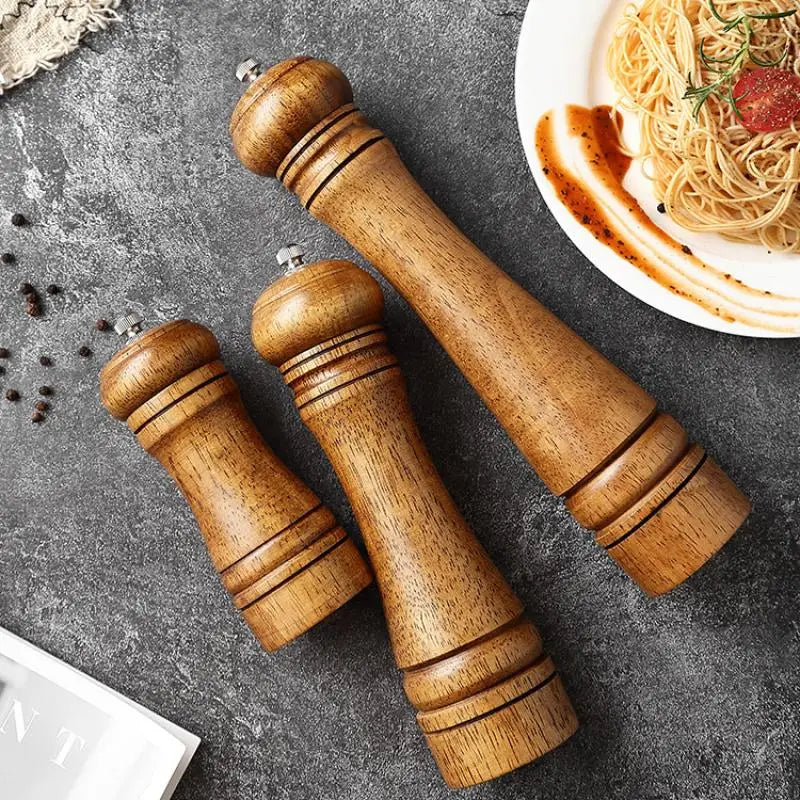 Set of wooden pepper mills on a gray surface with a plate of pasta in the background.