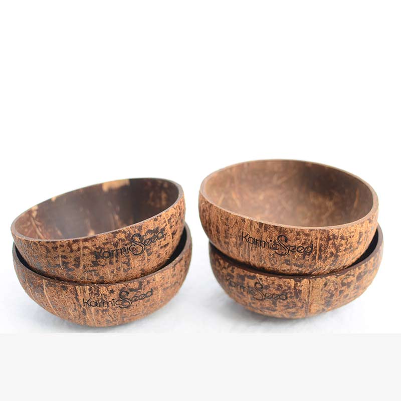 Four handcrafted coconut bowls on a natural wooden surface, surrounded by fresh tropical fruits. Each bowl has a smooth, polished finish with no branding or logo. Earthy and minimal.