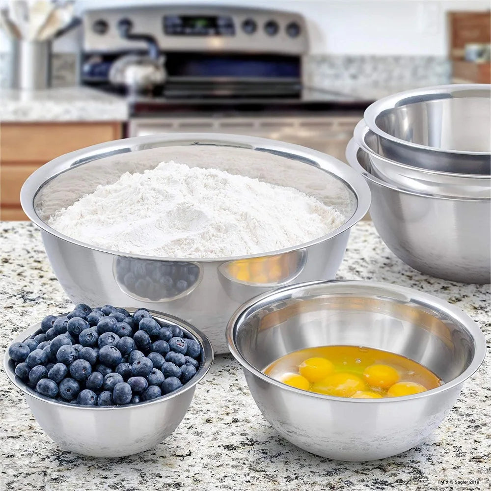 Set of stainless steel bowls with flour, blueberries, and eggs on a kitchen counter.