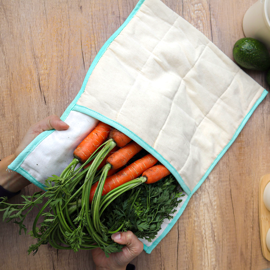Person holding a reusable produce bag with carrots and greens on a wooden table.
