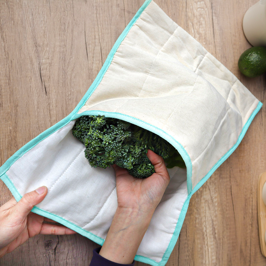 Person holding a white cloth with green vegetables inside on a wooden surface
