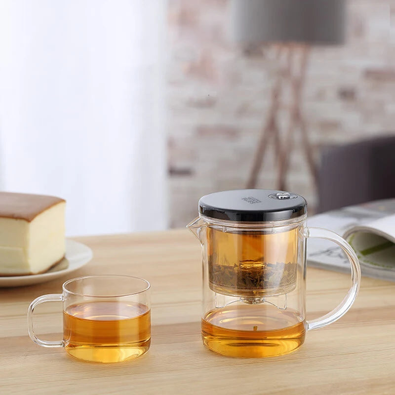 Clear glass teapot and mug with tea on a wooden table, with a blurred background