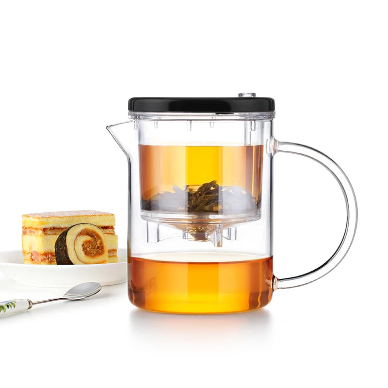 Clear glass teapot with a black lid and handle, filled with tea, on a white background.