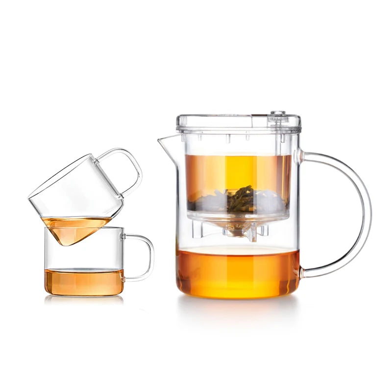 Clear glass teapot with handle and two clear cups filled with tea on a white background
