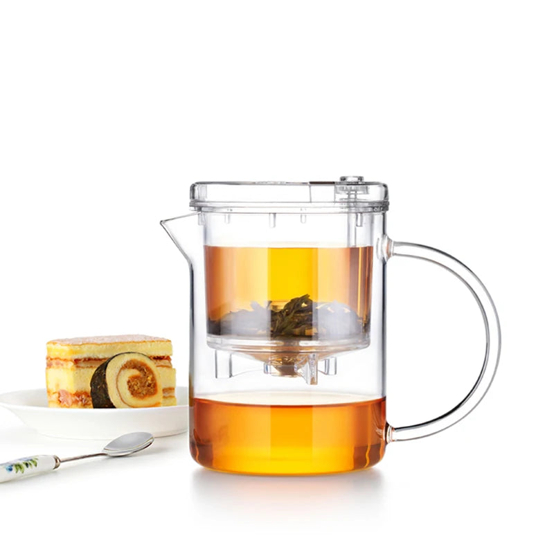 Clear glass teapot with tea and a cake on a white background