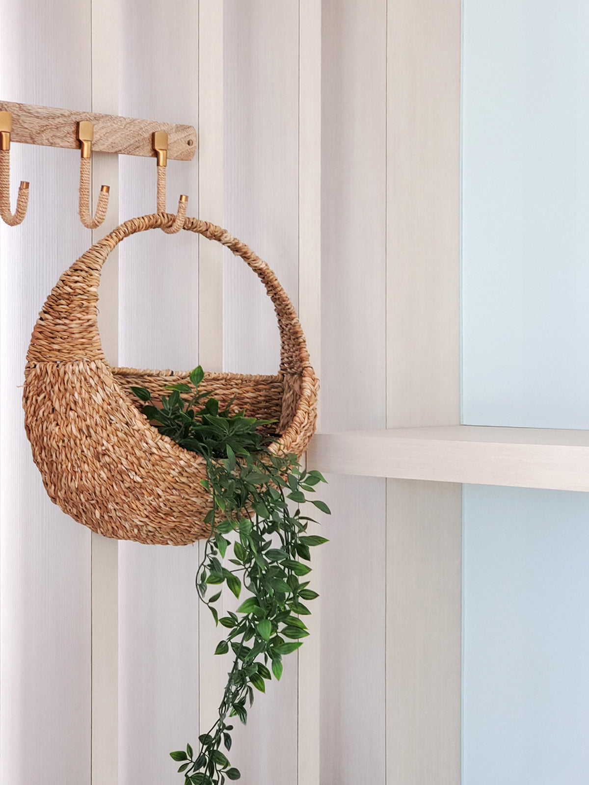 Savar woven seagrass wall basket with decorative wooden hooks and trailing green plant - angled lifestyle photo showing home organization